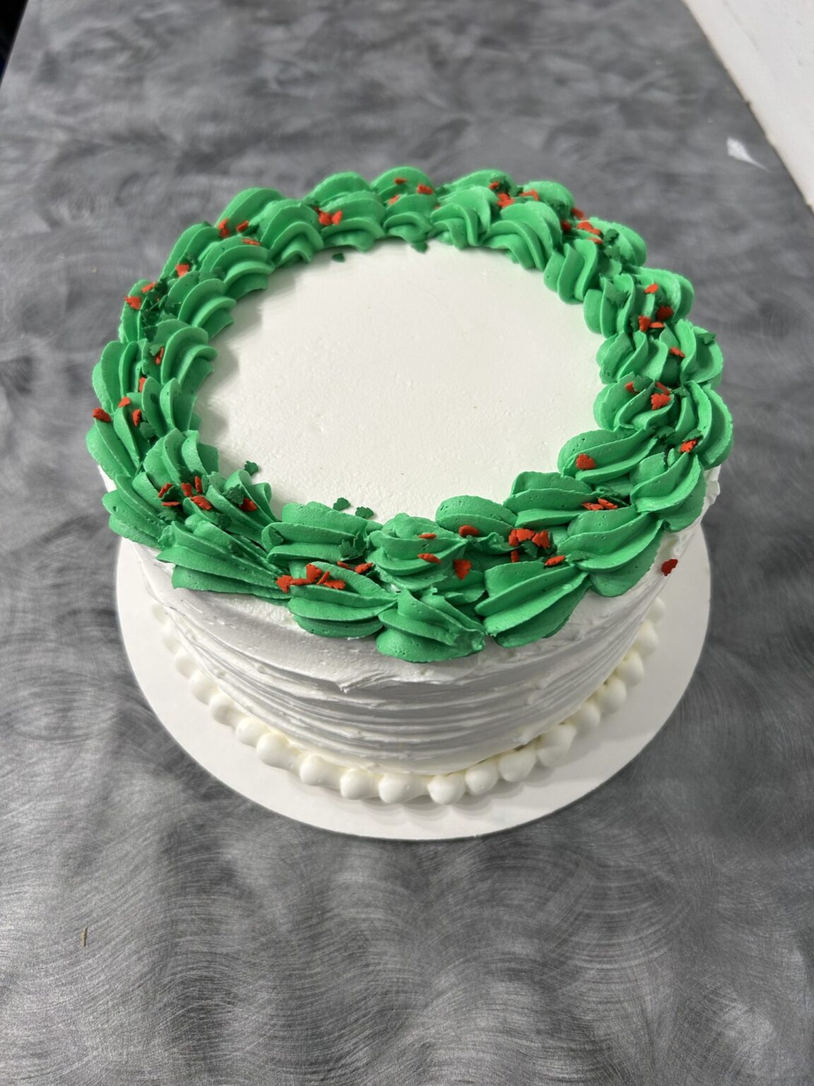 Round cake with green frosting border on table.
