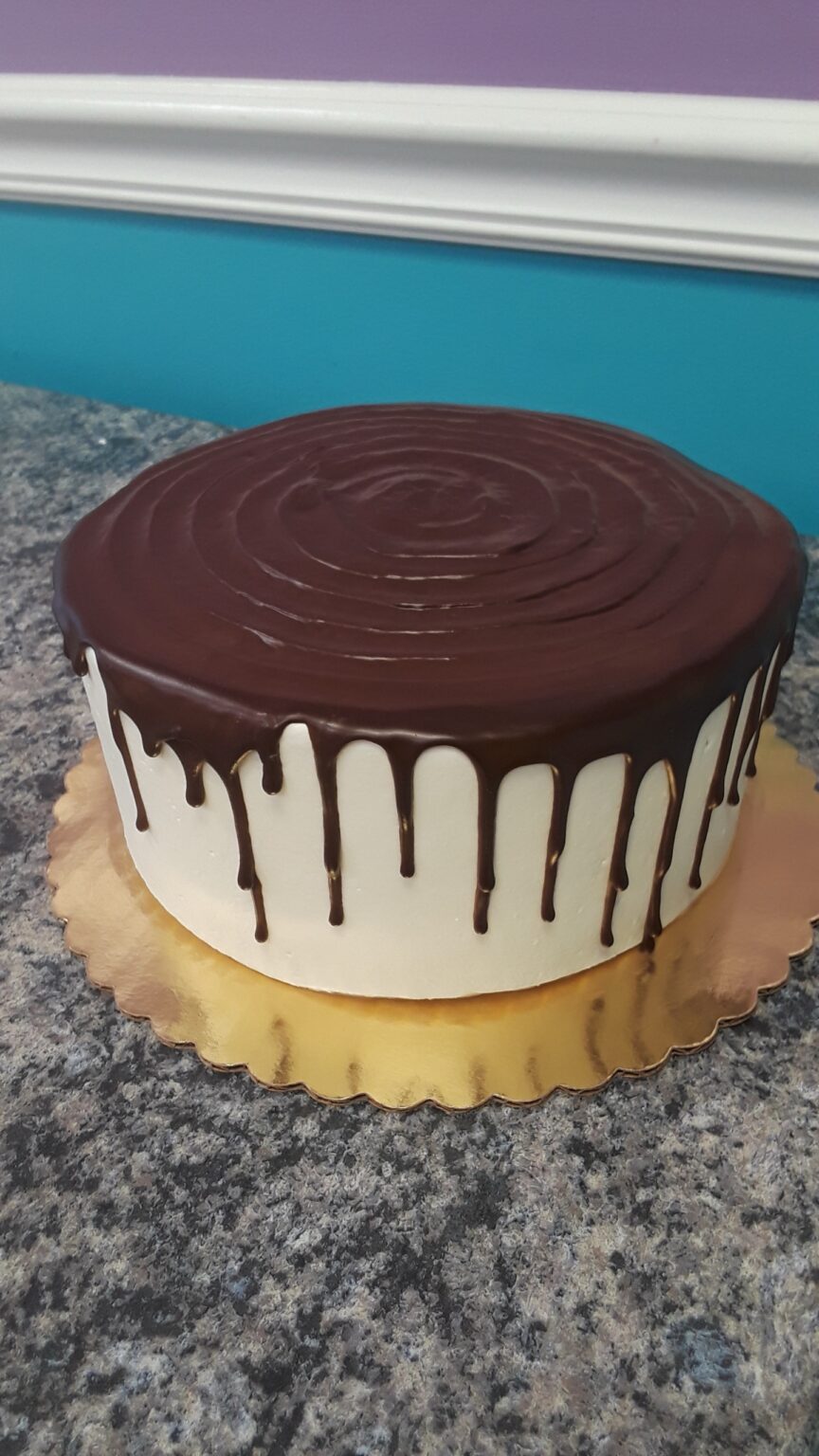 Chocolate drip cake on a golden stand.